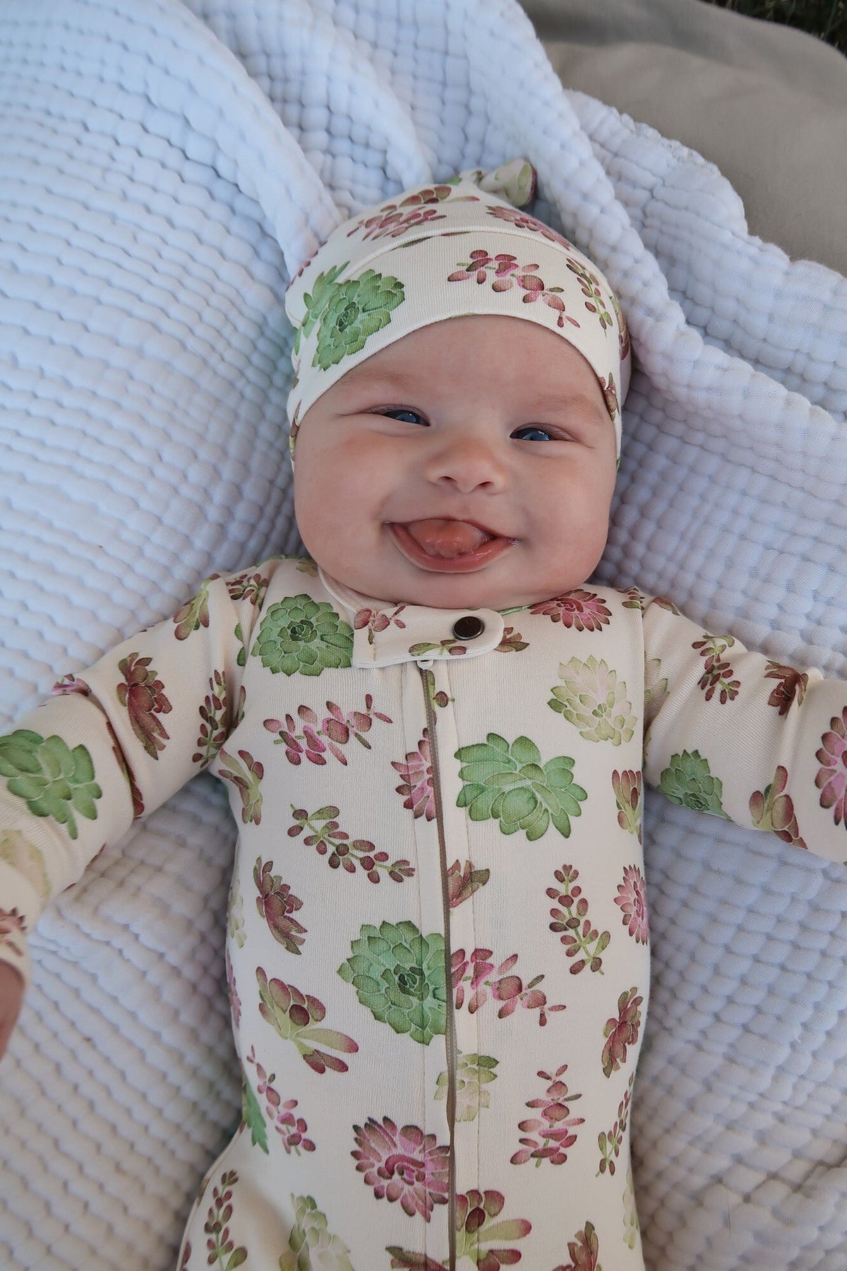 Baby wearing a floral outfit and hat, lying on a textured blanket