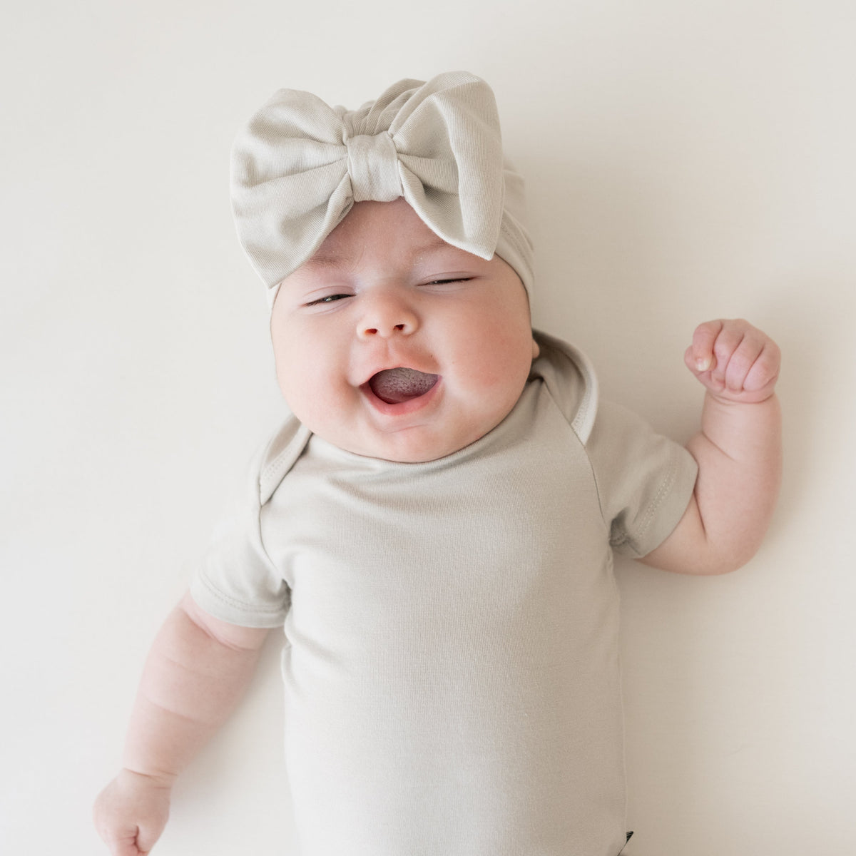 Baby wearing a light gray bow headband and onesie on a white background