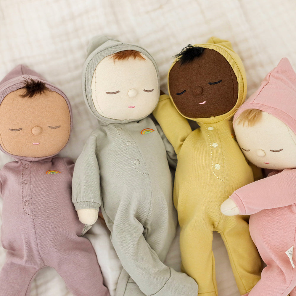 Four dolls in different colored onesies lying on a soft surface