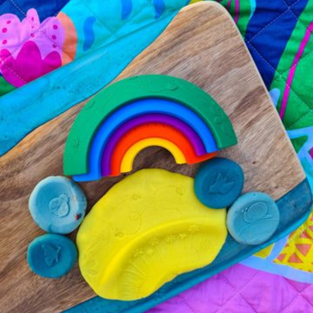 Colorful rainbow-shaped play dough on a wooden board with a colorful background