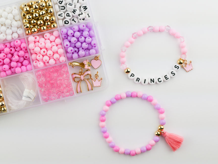 Princess Party DIY Bracelet Kit featuring a compartment storage box filled with colorful beads, alphabet letter beads, and charms next to two completed pink, purple, and gold beaded bracelets, including one spelling "PRINCESS" with a small crown and tassel charm.