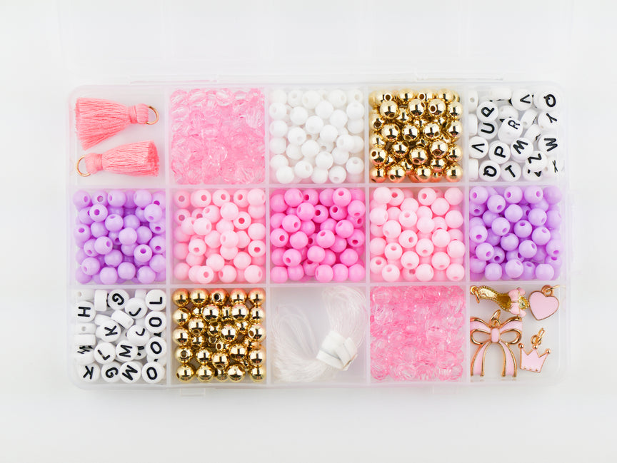 Princess Party DIY Bracelet Kit storage box shown from above, filled with sorted compartments of pink tassels, white and pink round beads, gold spacer beads, alphabet letter beads, and elastic cording.