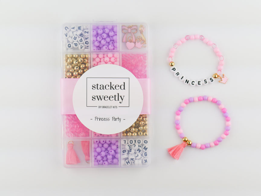 Princess Party DIY Bracelet Kit featuring a compartment storage box with a "stacked sweetly - Princess Party" label, filled with colorful beads, alphabet letter beads, and charms, next to two completed pink, purple, and gold beaded bracelets, including one spelling "PRINCESS" with a small crown and tassel charm.