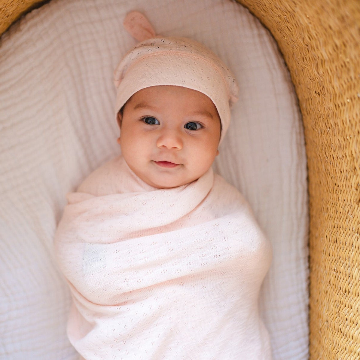 Baby wrapped in a pink blanket and hat, lying in a woven basket.