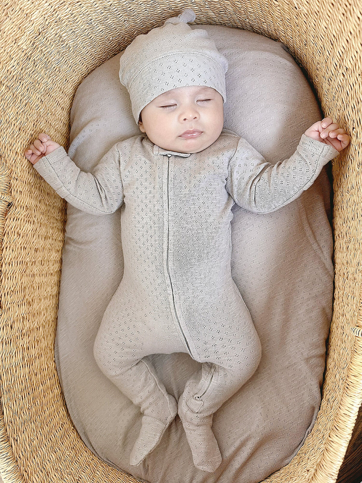 Baby in a textured outfit and hat lying on a soft surface