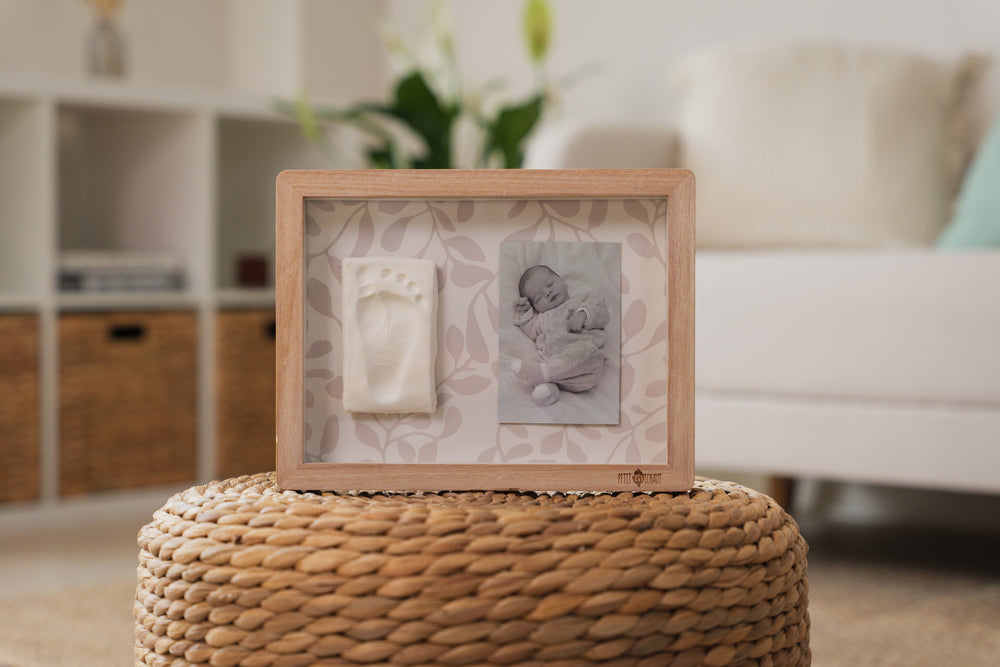 Wooden photo frame with baby milestone cards on a woven ottoman in a living room.