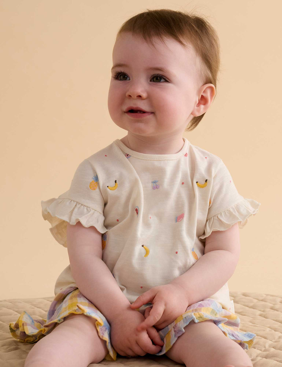 Baby wearing a white outfit with colorful patterns on a beige background