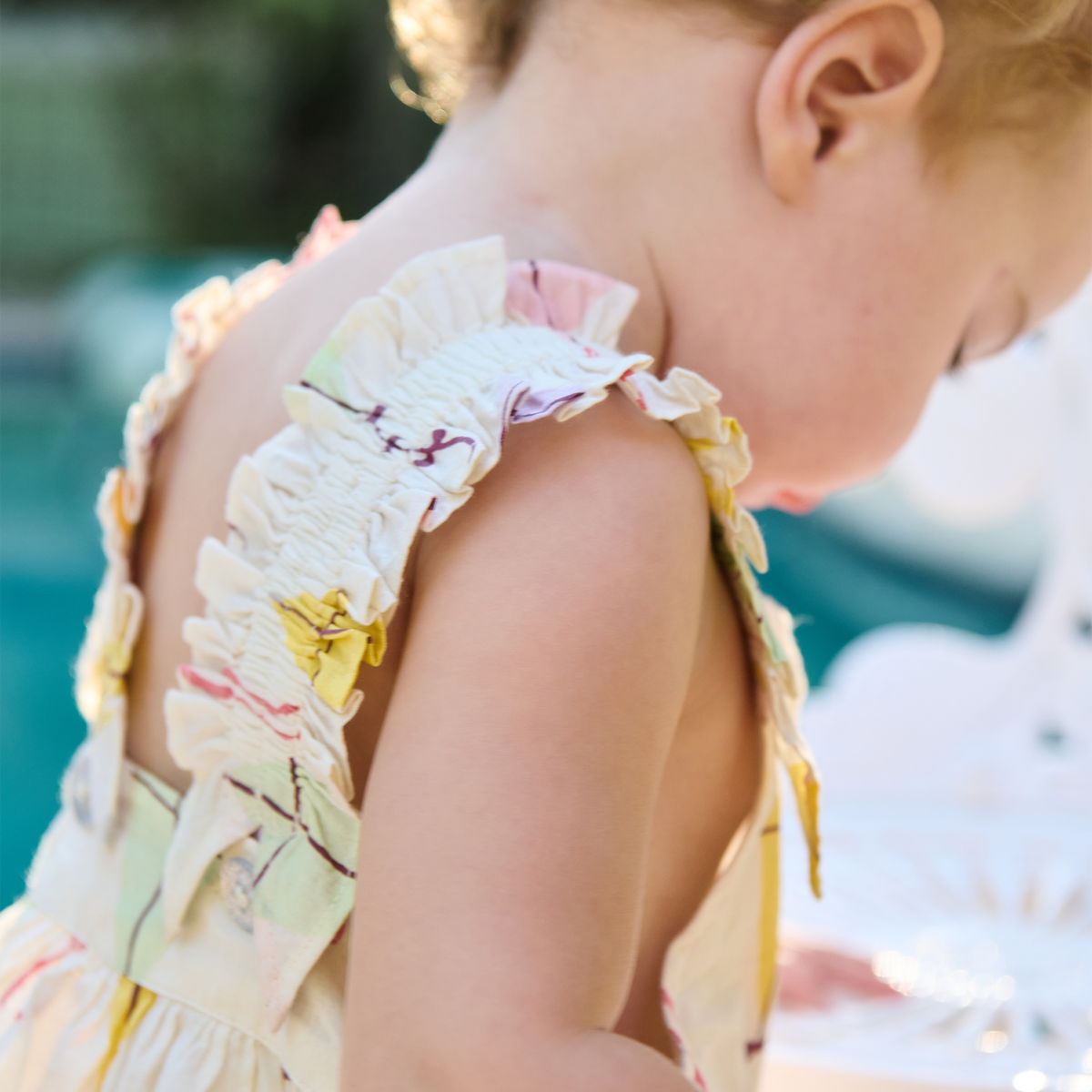 Child wearing a colorful dress with ruffled details, blurred outdoor background