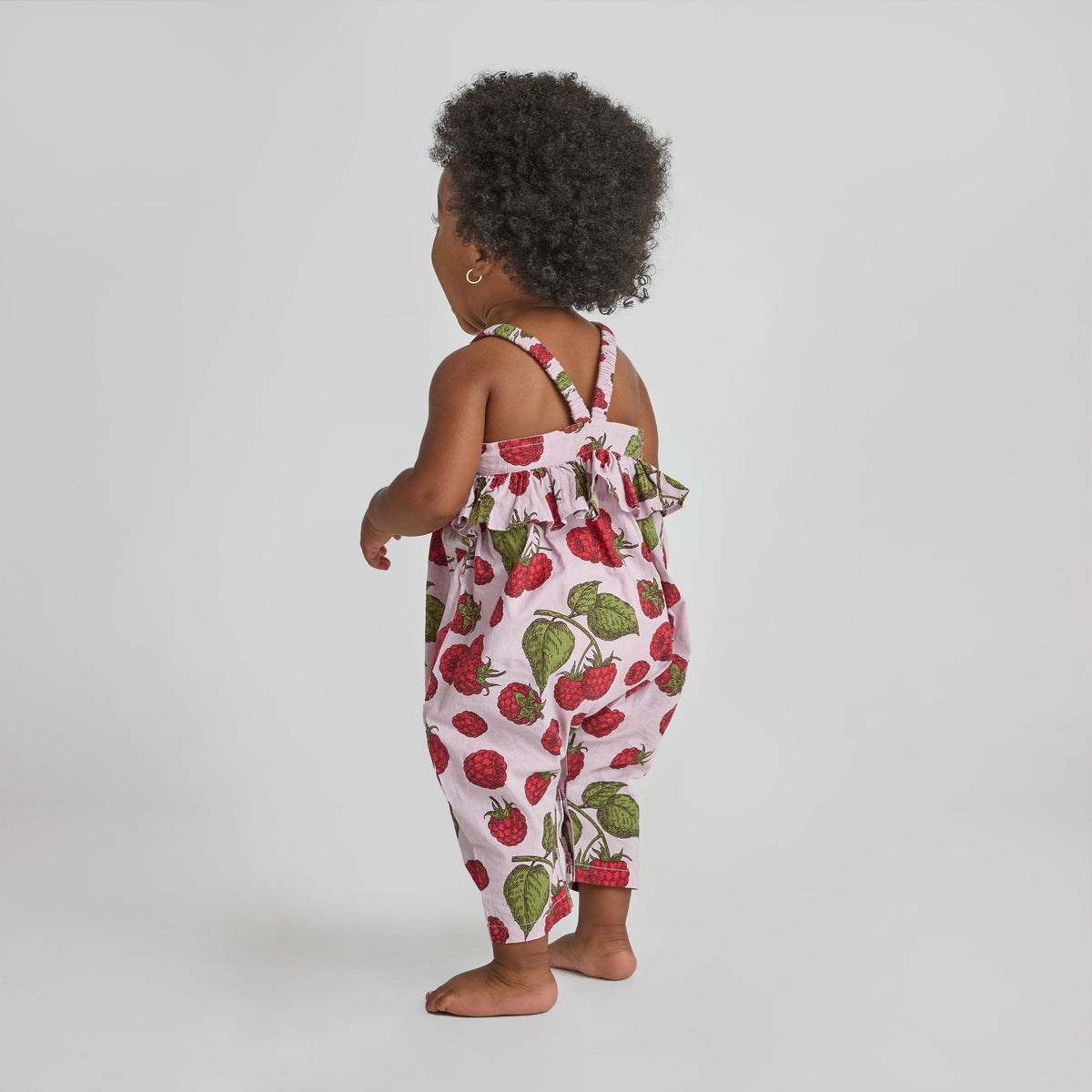 Child wearing a strawberry print romper on a plain background
