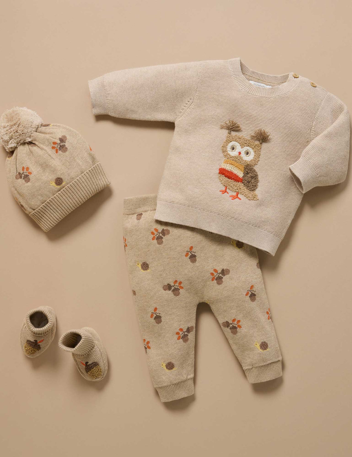 Baby outfit set with sweater, pants, hat, and shoes on a beige background