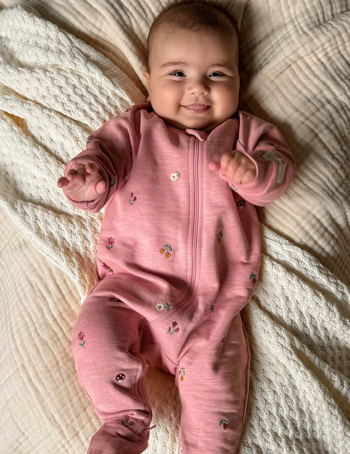 Baby in a pink onesie lying on a textured blanket