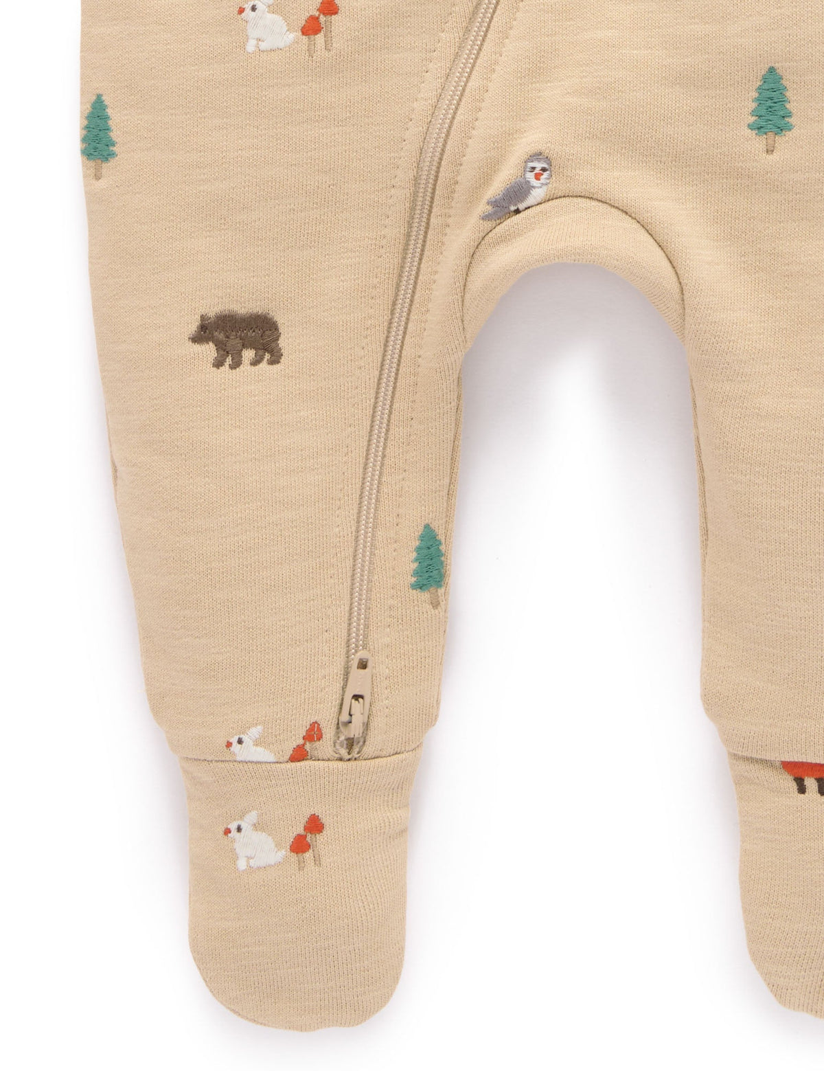 Close-up of a baby footed sleeper in a warm beige heathered fabric, featuring a small woodland animal print including a bear, owl, fox, and pine tree, with a zippered leg.