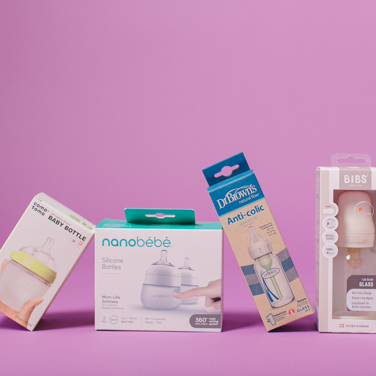 Four baby bottle packaging boxes arranged on a solid pink-purple studio background. The boxes include Little Baby Bottle, nanobébé Silicone Bottles, Dr.