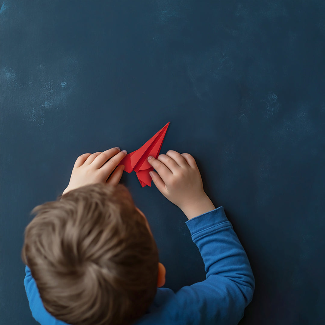 Child holding a red paper airplane against a dark blue background
