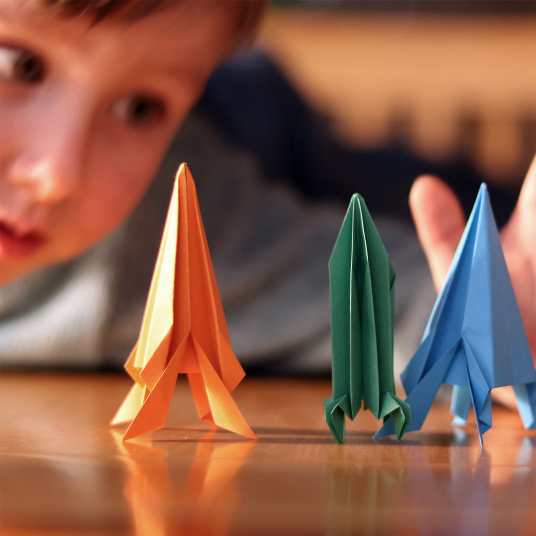 Child looking at three colorful paper airplanes on a wooden surface