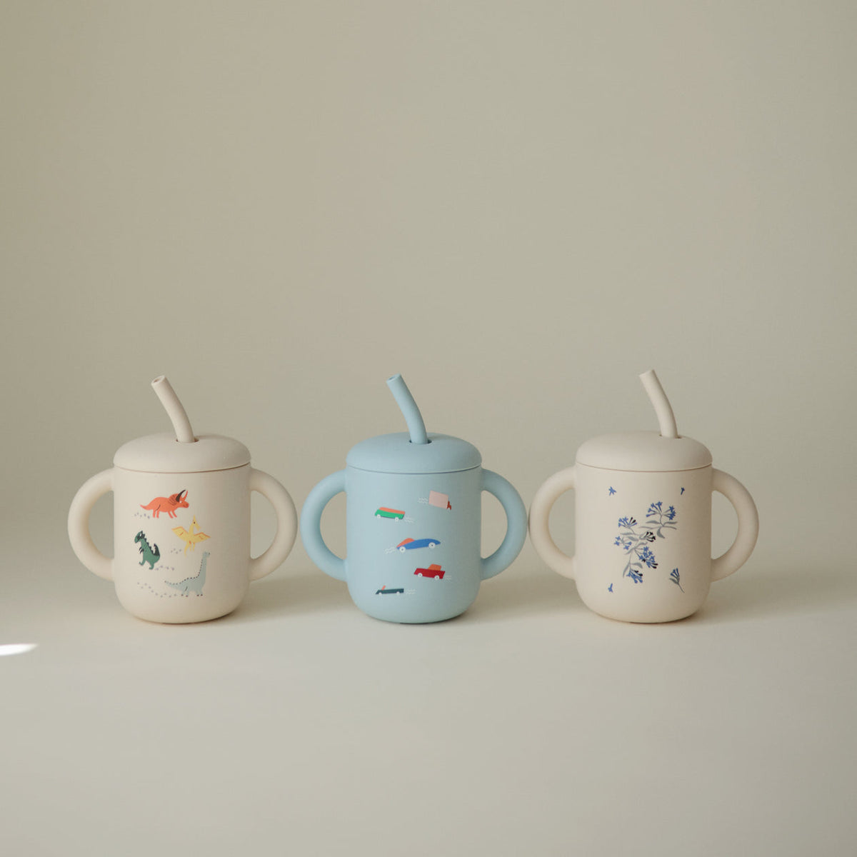 Three children's sippy cups with lids and straws on a plain background
