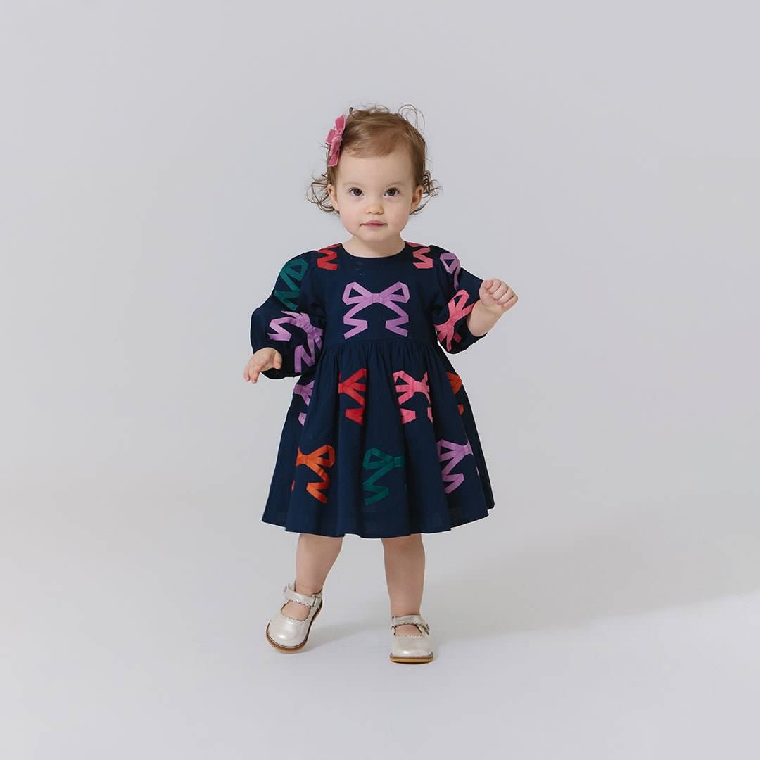 Child wearing a navy dress with colorful bow patterns on a white background