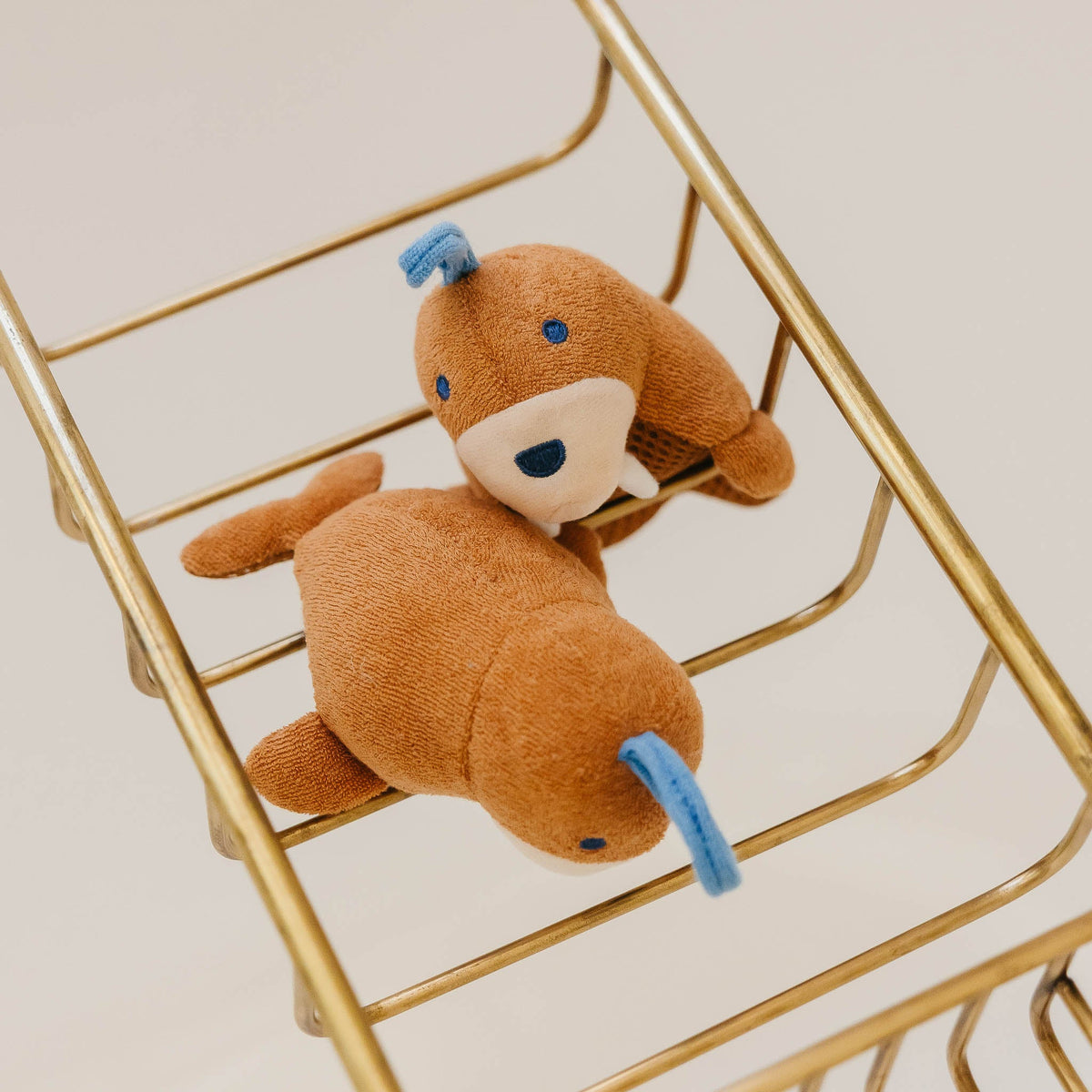 Small brown teddy bear with blue accents sitting inside a gold metal cart.