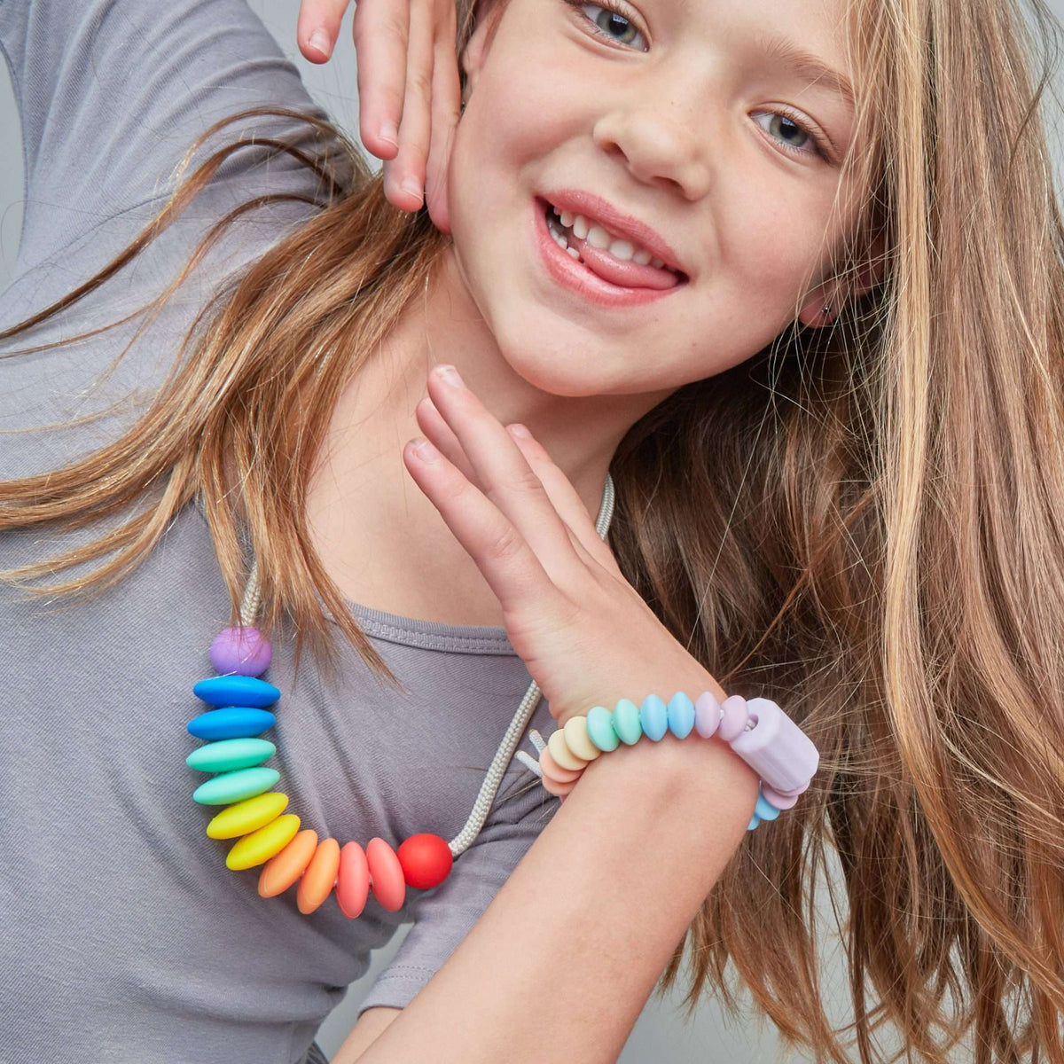 Young girl wearing a colorful beaded necklace and bracelet on a plain background