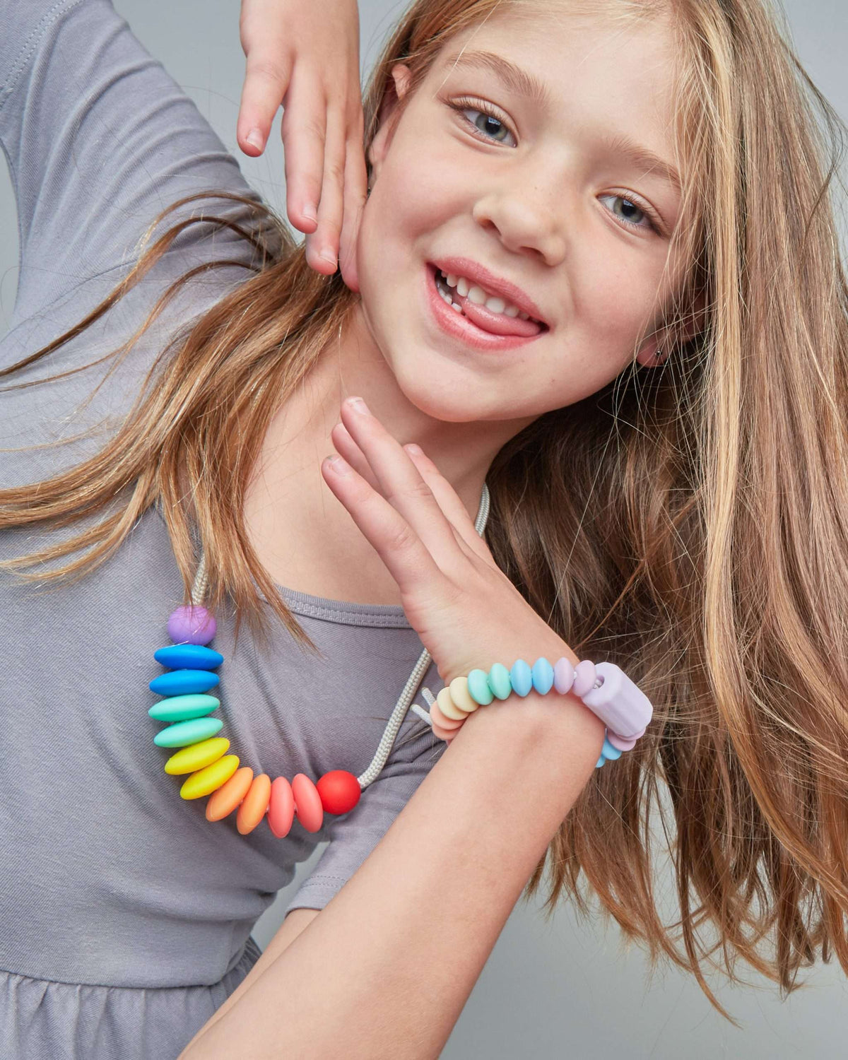 Young girl wearing a colorful beaded necklace and bracelet on a plain background