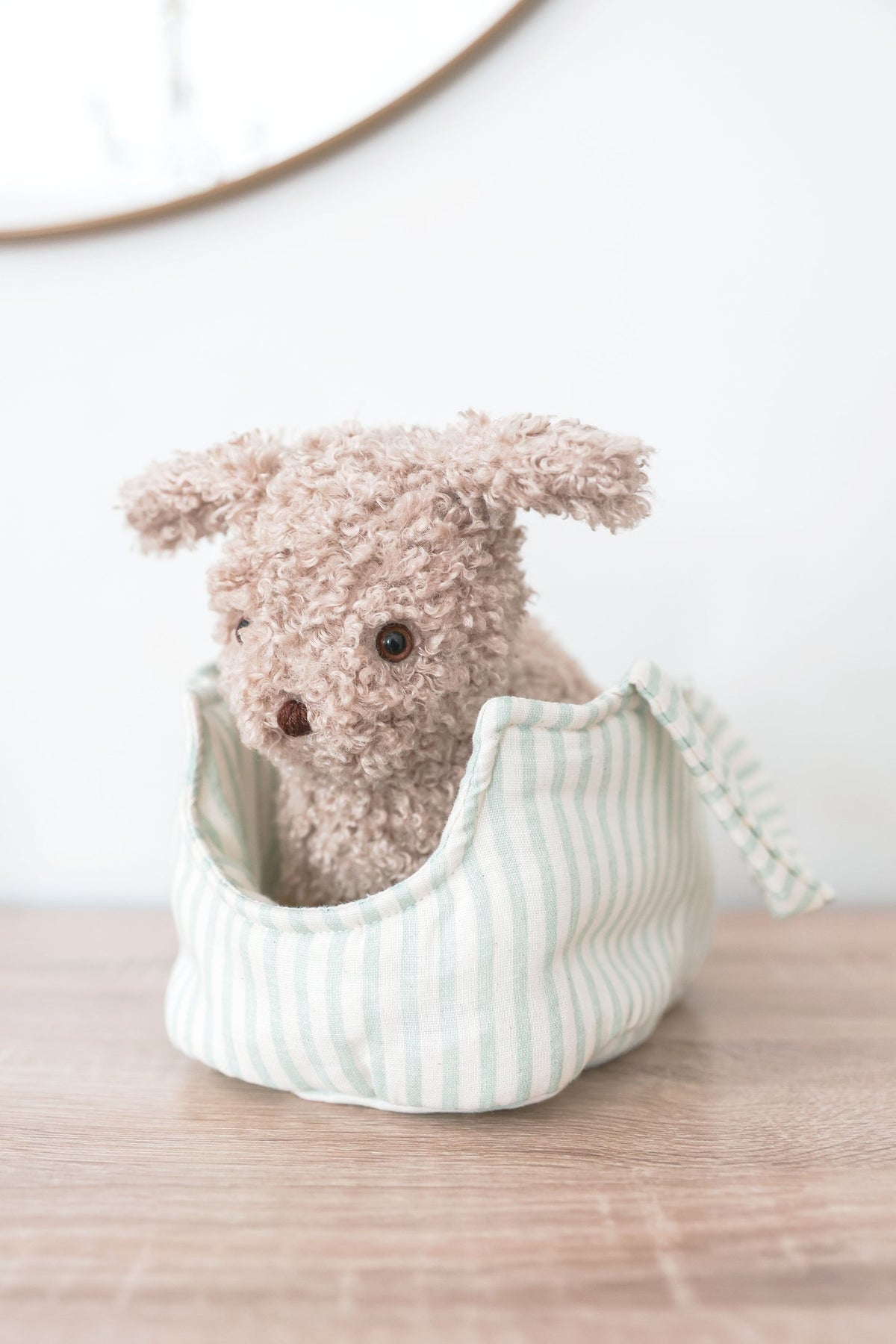 Small plush dog toy in a white container on a wooden surface with a light background