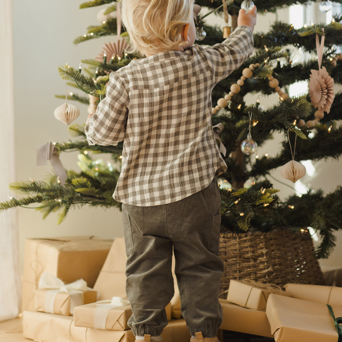 Child decorating a Christmas tree with ornaments, surrounded by wrapped gifts.