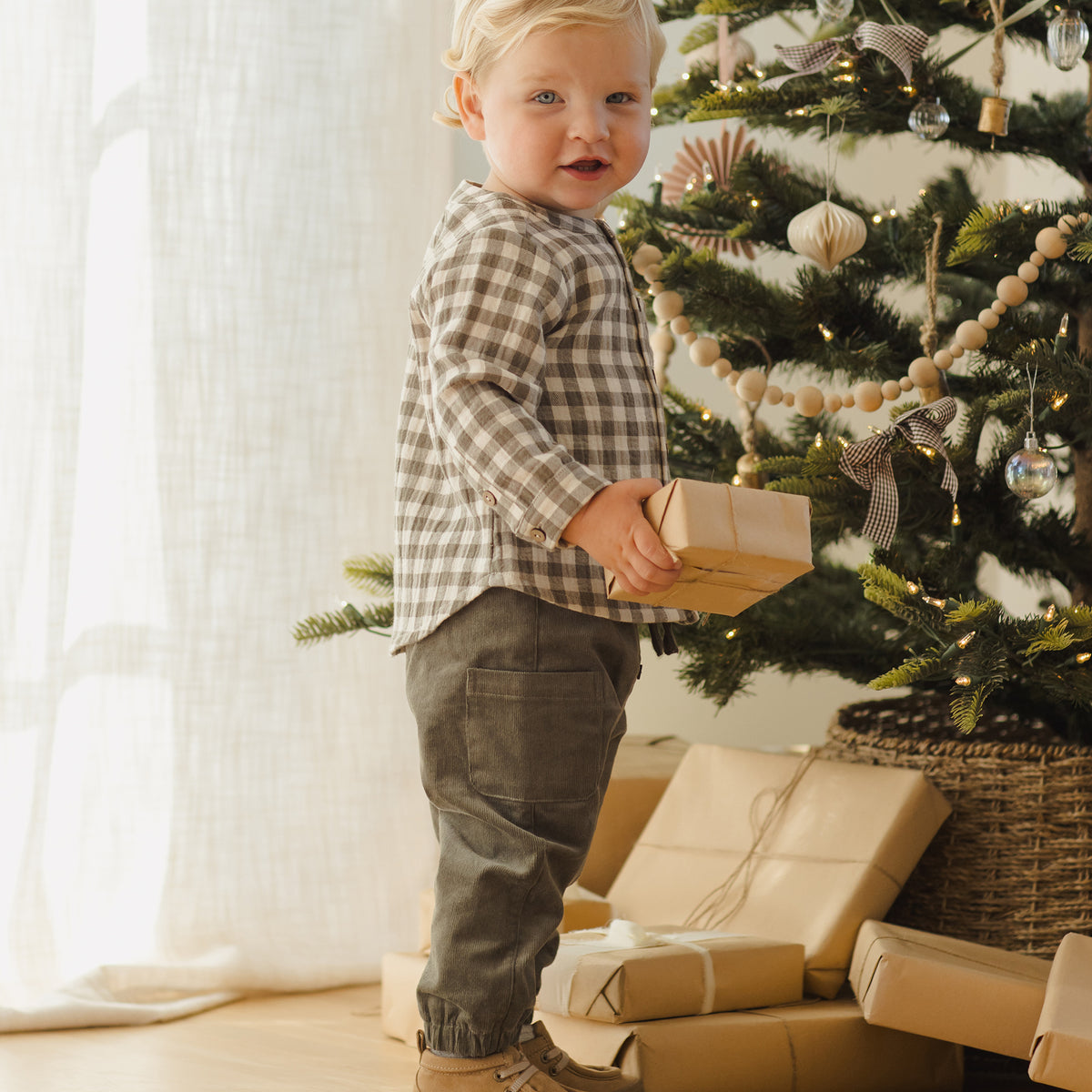 Child standing next to a decorated Christmas tree with presents underneath.