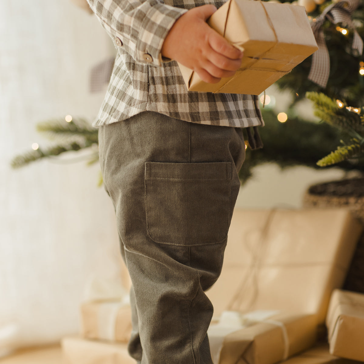 Child holding a gift box in front of a decorated Christmas tree.