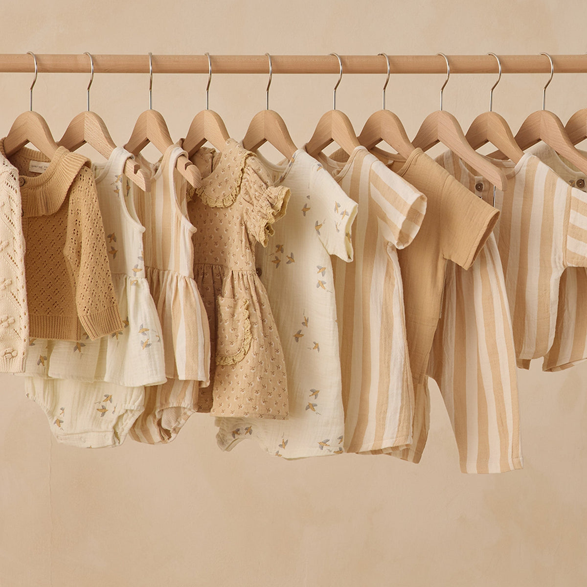 Row of children's clothing on hangers against a beige wall