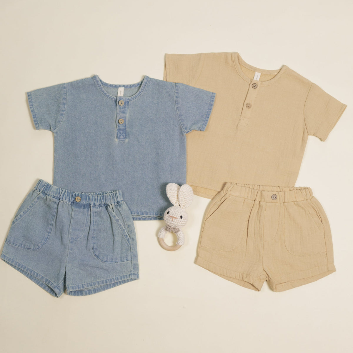 Two children's outfits, one blue and one beige, with matching shorts and a toy on a light background.