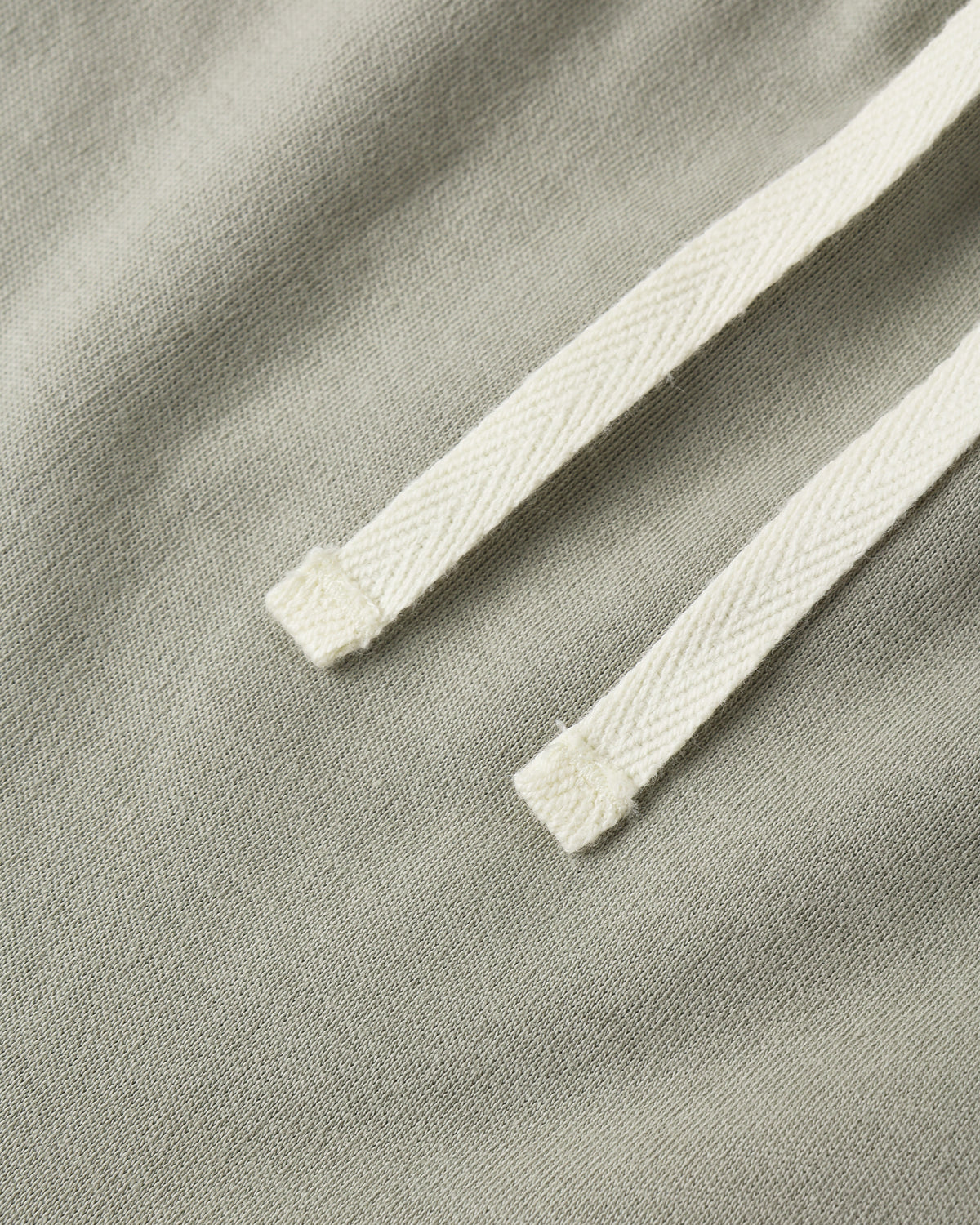 Close-up of a light sage green fabric with a contrasting off-white braided drawstring.