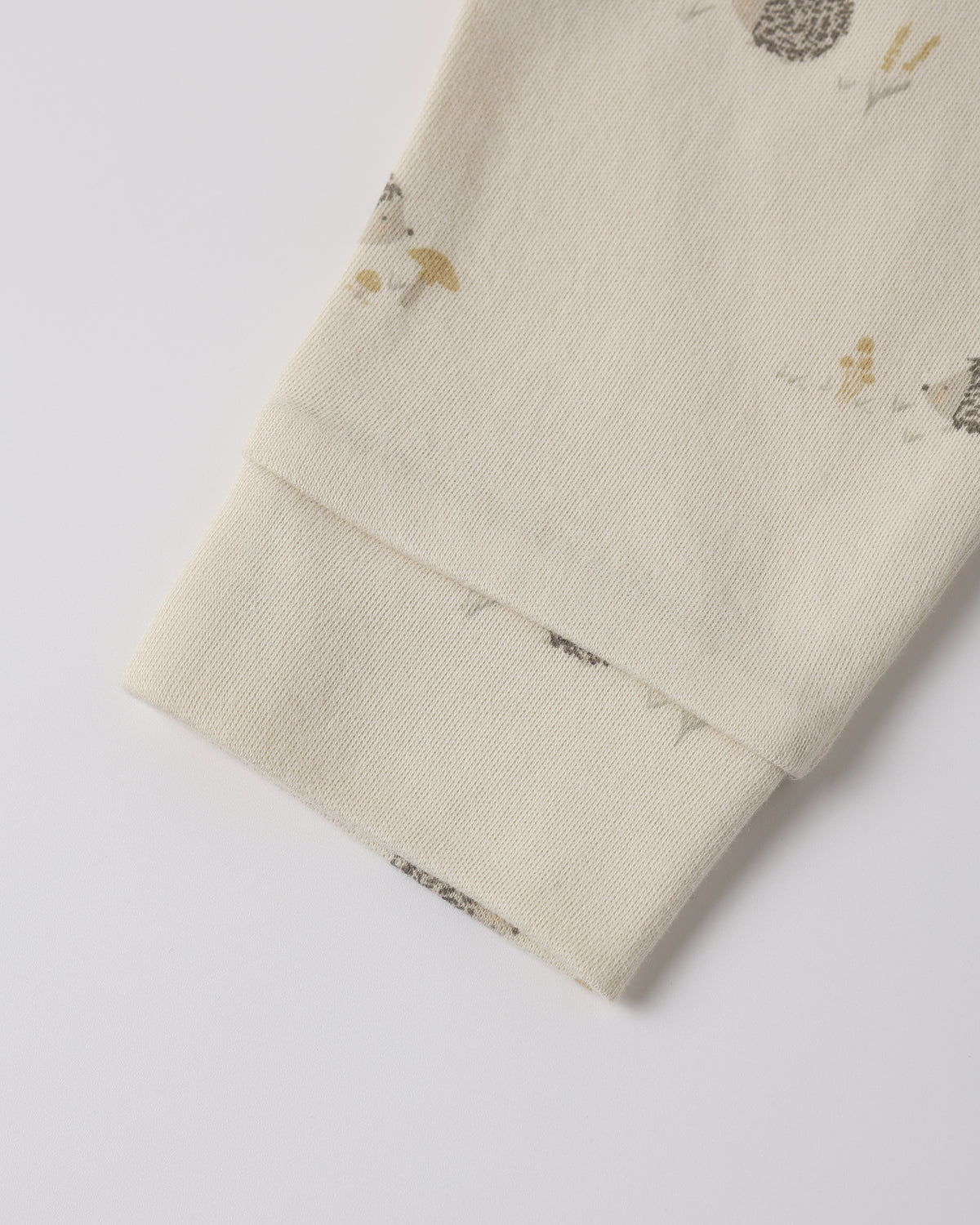 Close-up of a cream-colored fabric sleeve or cuff with a small woodland print of hedgehogs, mushrooms, and birds, finished with a ribbed elastic cuff.