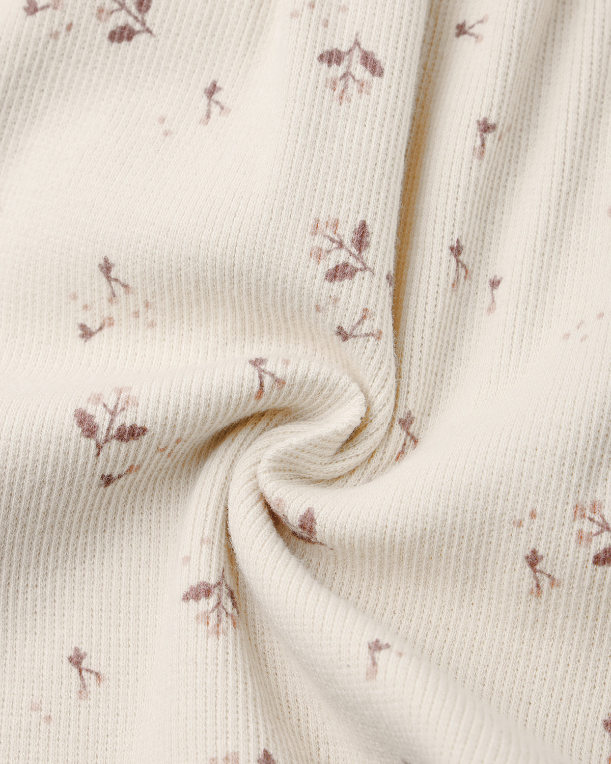 A close-up of cream-colored ribbed fabric with a delicate, small-scale dusty rose floral print, styled with a central swirl to show texture and drape.