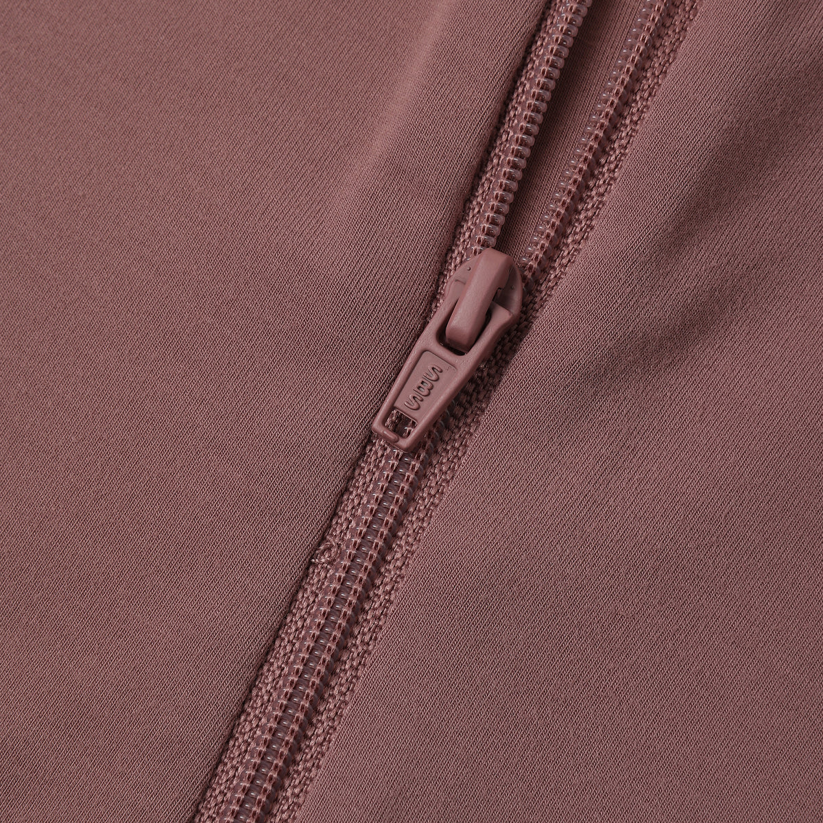 Close-up of a dusty rose pink zippered garment, showing the fabric texture and a matching pull tab with the brand name 'SOL'S' visible.