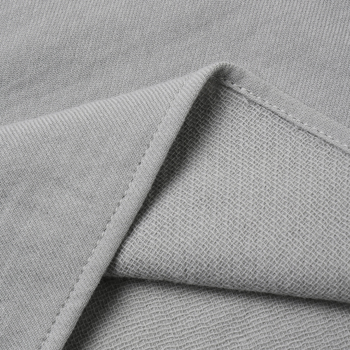 Close-up of light gray woven fabric with a folded corner showing the texture and stitching.