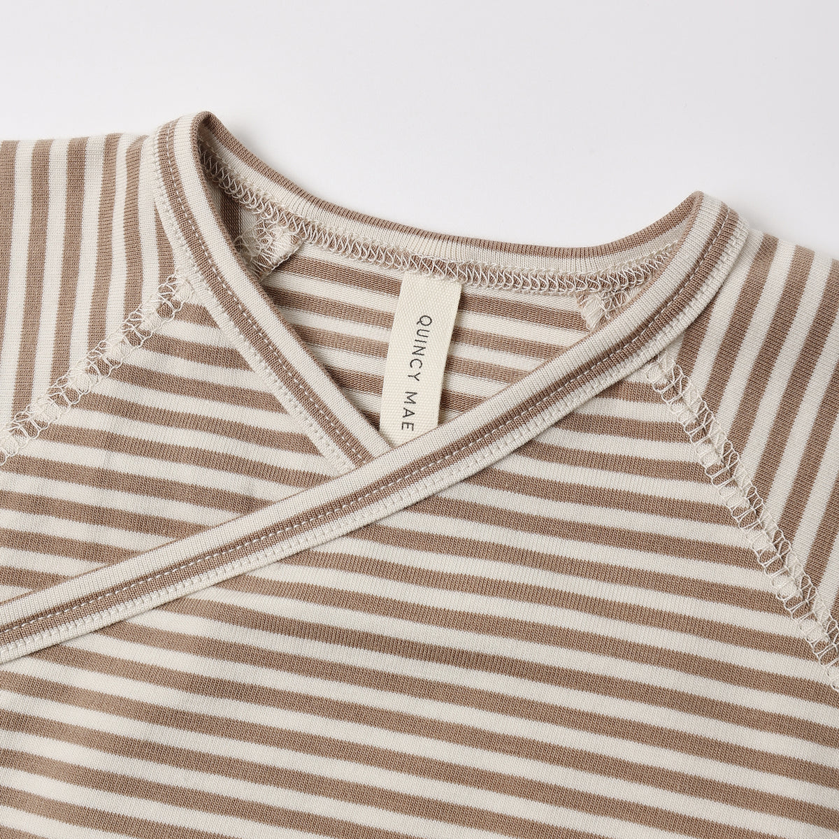 Close-up of a baby wrap top with horizontal beige and off-white stripes, featuring a V-neck and a visible 'CONCEPT MATE' brand tag.