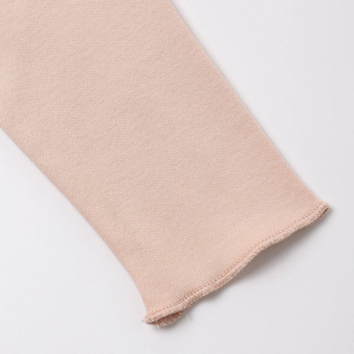 A close-up of a light blush pink knit fabric sleeve or cuff with a frayed hem, shown on a clean white background.