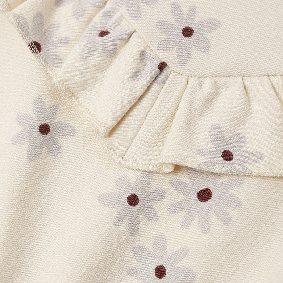 Close-up of a cream-colored fabric garment featuring a ruffled neckline and an all-over daisy print with light gray petals and dark brown centers.