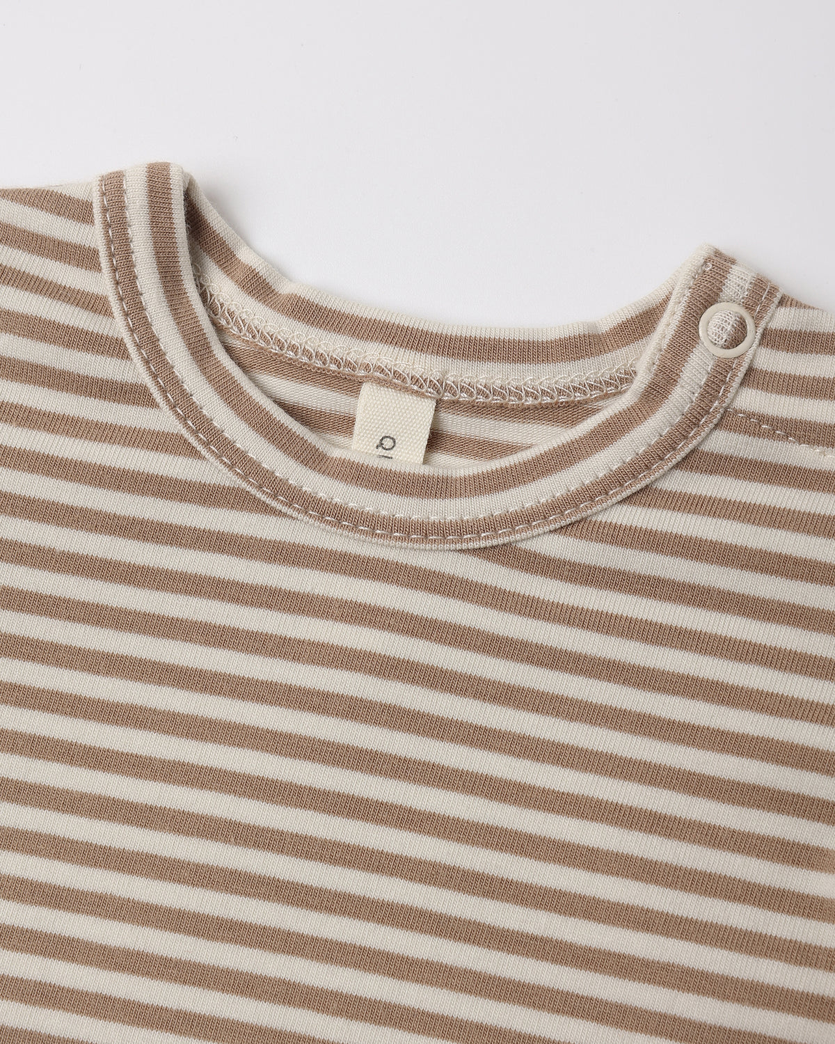Close-up of a striped baby top with a cream and light brown horizontal stripe pattern, featuring a ribbed crew neck and a small white tag.