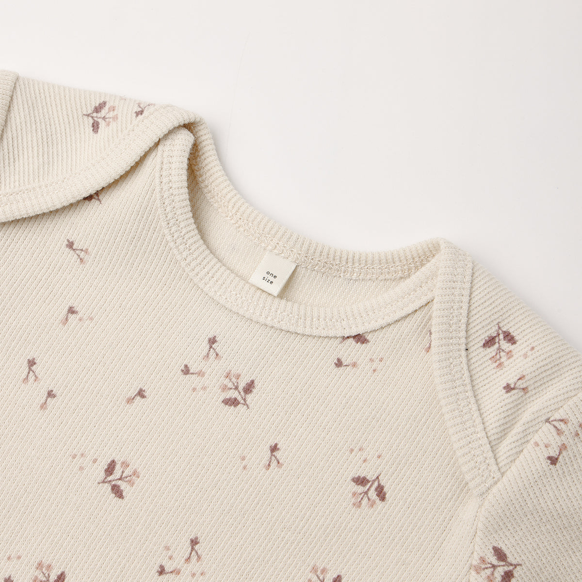 Close-up of a cream-colored ribbed knit garment, likely a baby top or sweater, featuring a delicate brown floral and leaf pattern scattered across the fabric.