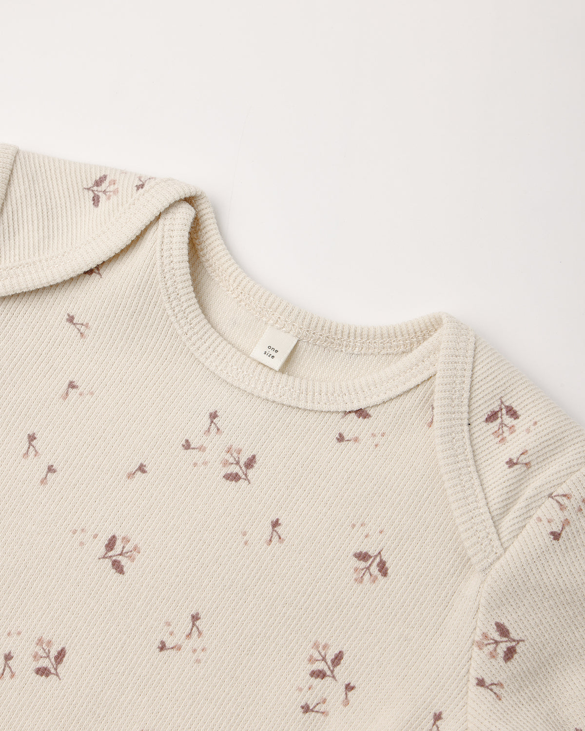 Close-up of a cream-colored ribbed knit garment, likely a baby top or sweater, featuring a delicate brown floral and leaf pattern scattered across the fabric.