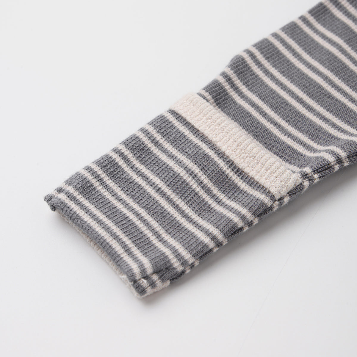 A close-up of a folded knit fabric item, likely a sock or sleeve cuff, featuring a gray and white striped pattern with a solid white stripe accent, on a light gray background.