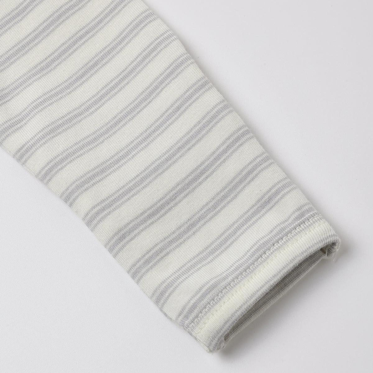 A close-up of a folded knit fabric sleeve or cuff with thin gray horizontal stripes on an off-white background, shown on a light gray studio background.