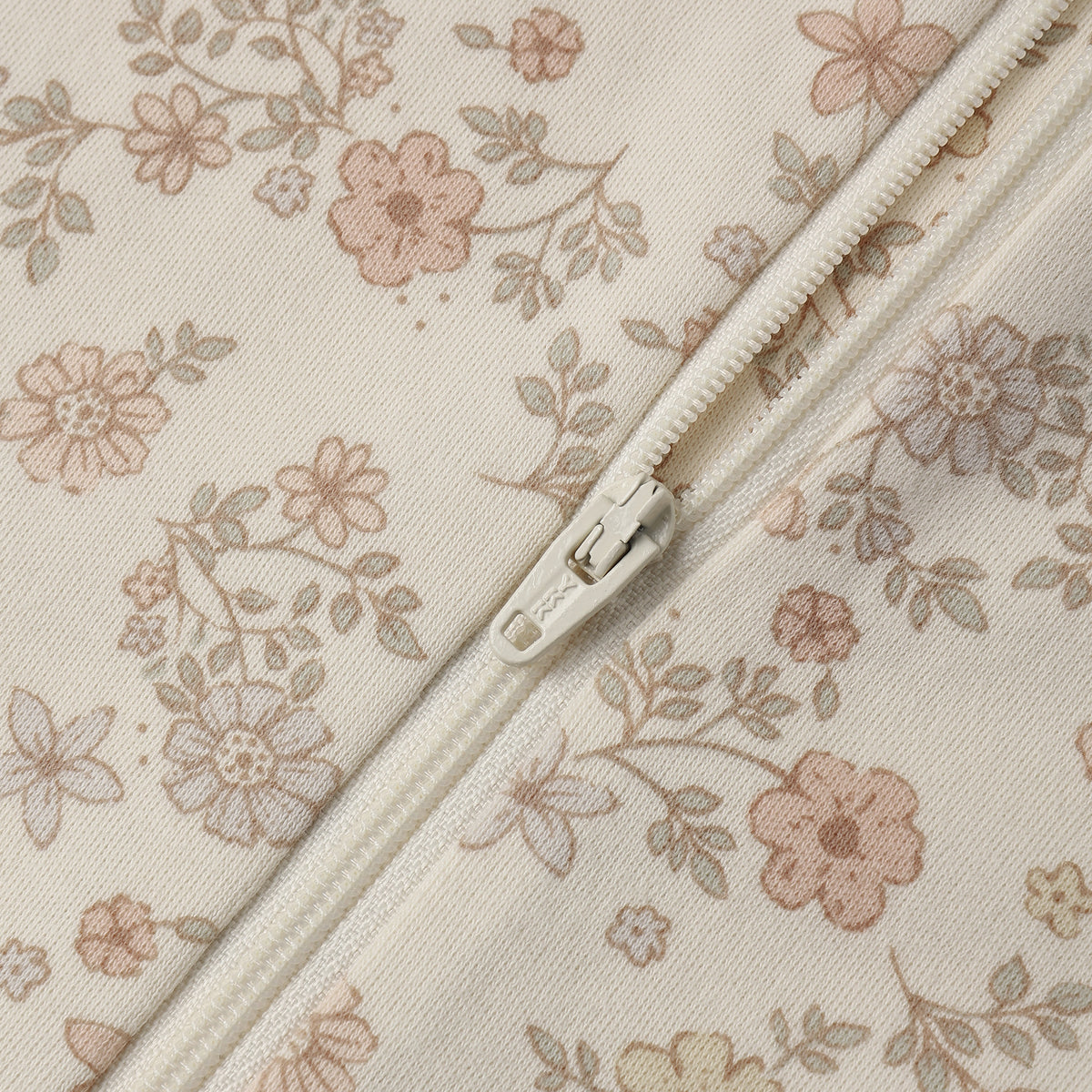 Close-up of a cream-colored fabric with a delicate pink and beige floral print, featuring a matching cream zipper running diagonally across the frame.