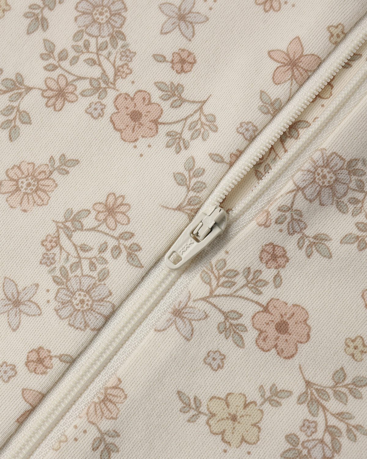 Close-up of a cream-colored fabric with a delicate pink and beige floral print, featuring a matching cream zipper running diagonally across the frame.