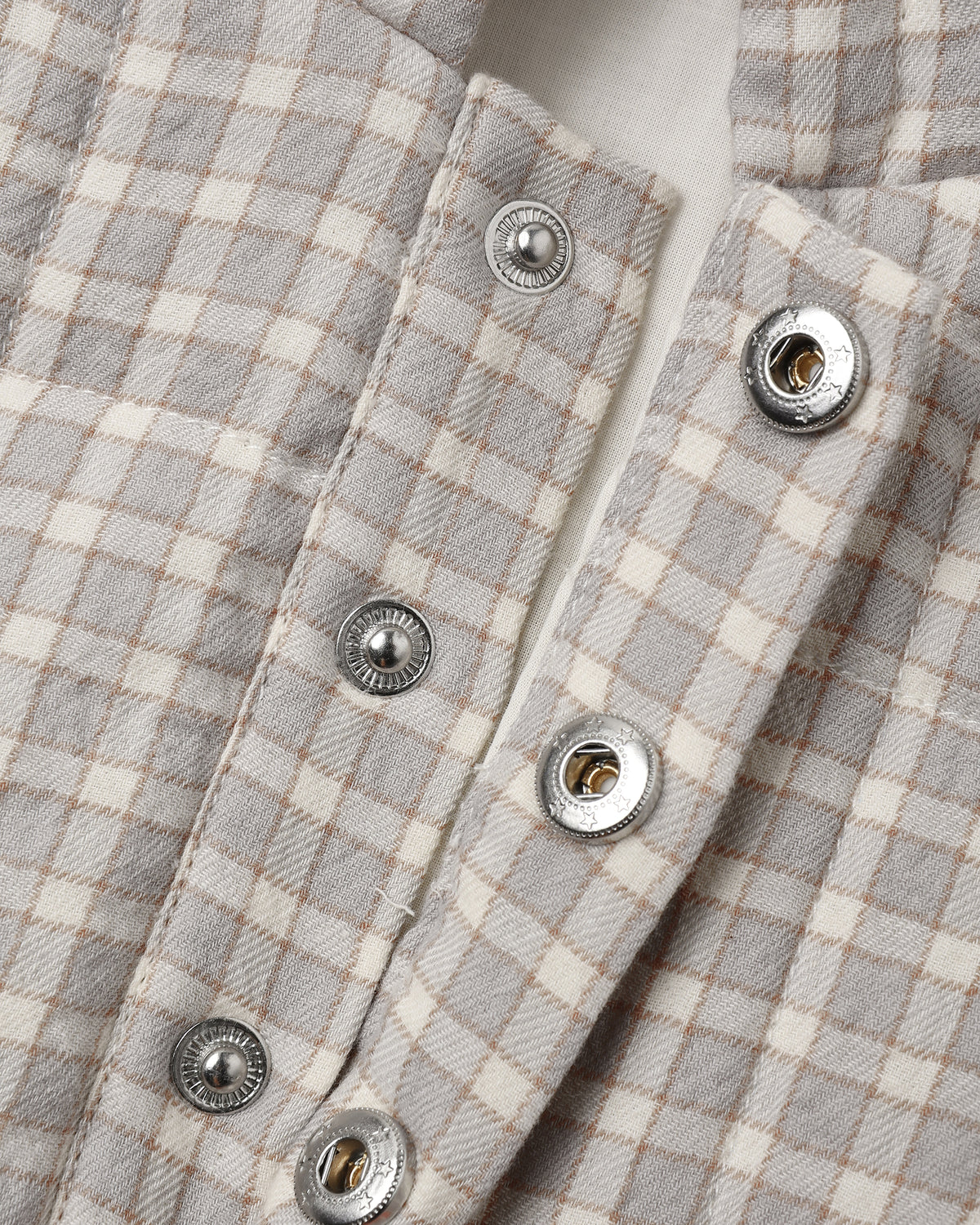 Close-up of a light gray and cream gingham plaid shirt with silver snap buttons.