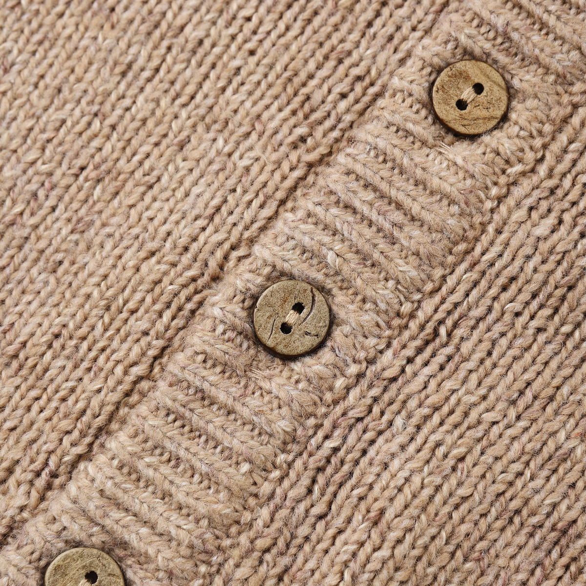 Close-up of a beige knit cardigan or sweater showing the ribbed texture and three round wooden buttons.