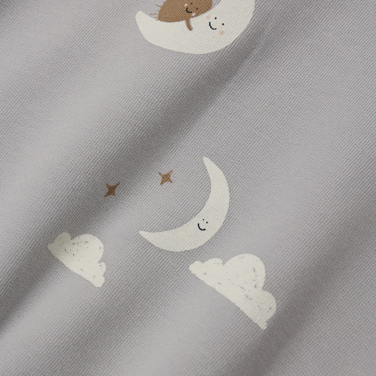 Close-up of a light gray fabric with a whimsical print of white crescent moons, small white clouds, and brown stars, each with a simple smiling face.