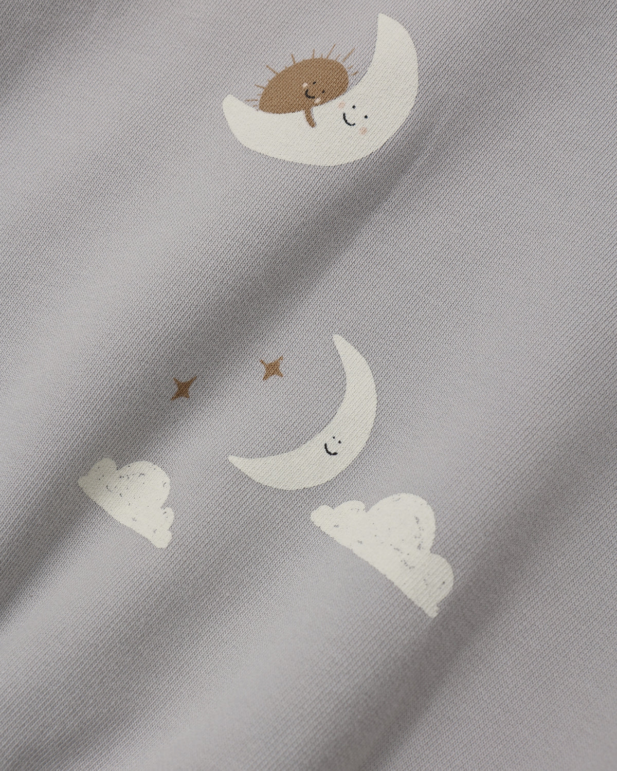 Close-up of a light gray fabric with a whimsical print of white crescent moons, small white clouds, and brown stars, each with a simple smiling face.