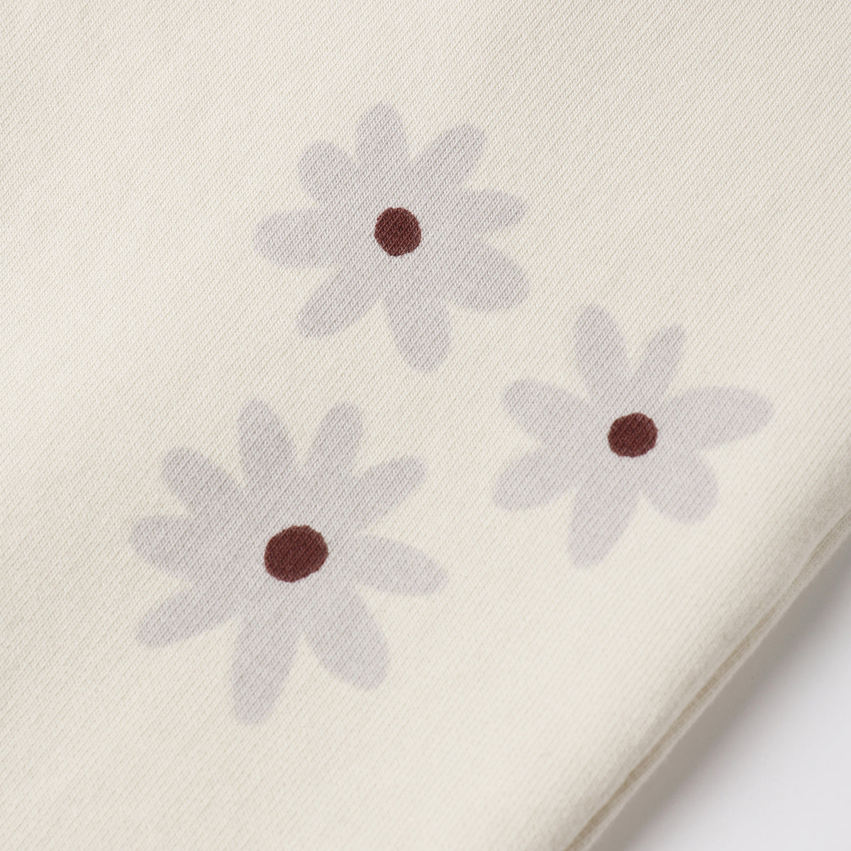 Close-up of a cream-colored fabric with three light gray daisy flowers printed on it, each with a small dark brown center.